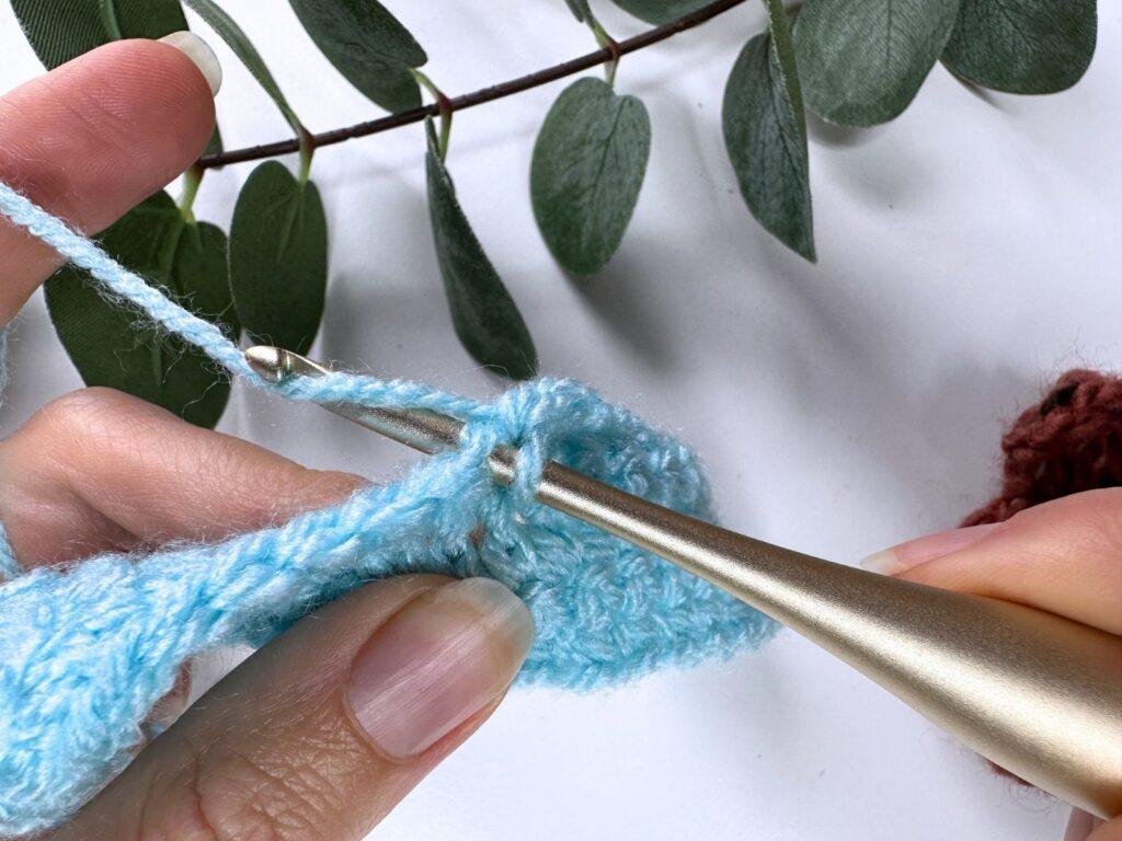A person is wrapping the yarn around the hook partway through a single crochet stitch 