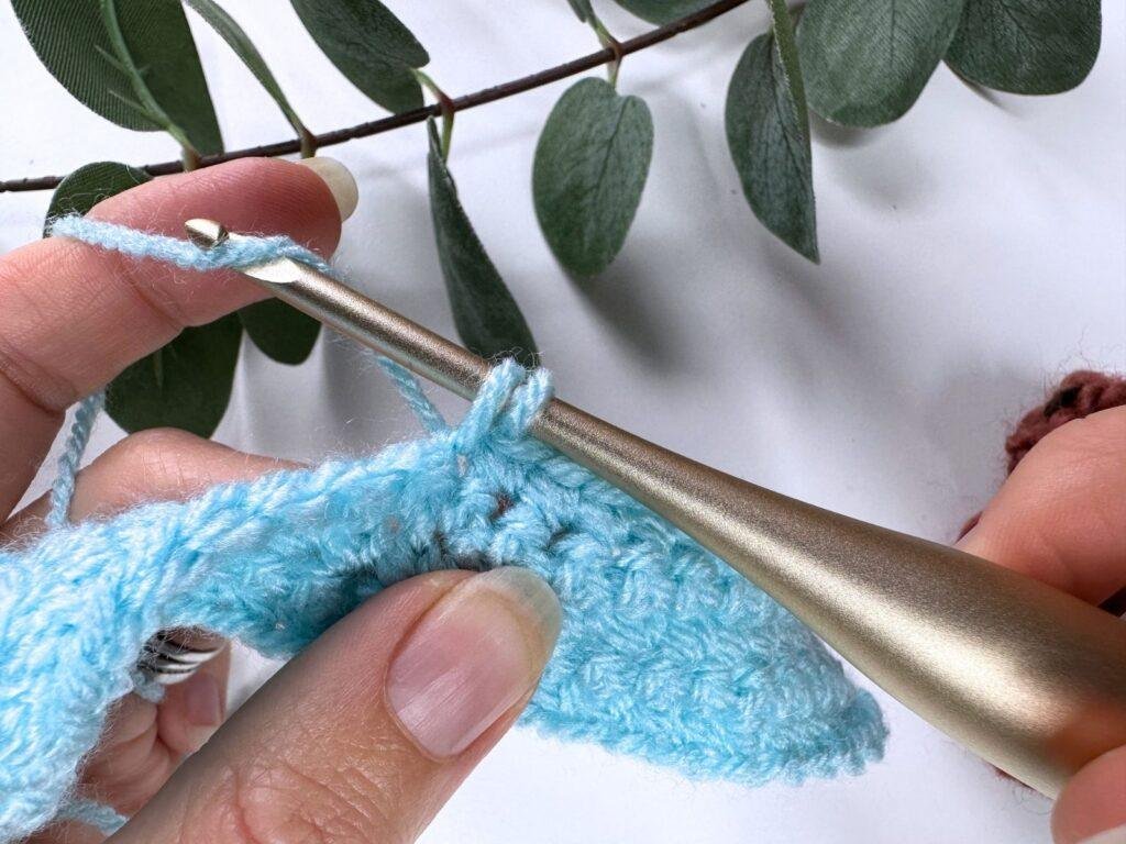 2 hands are wrapping the yarn around the hook again to complete the single crochet stitch