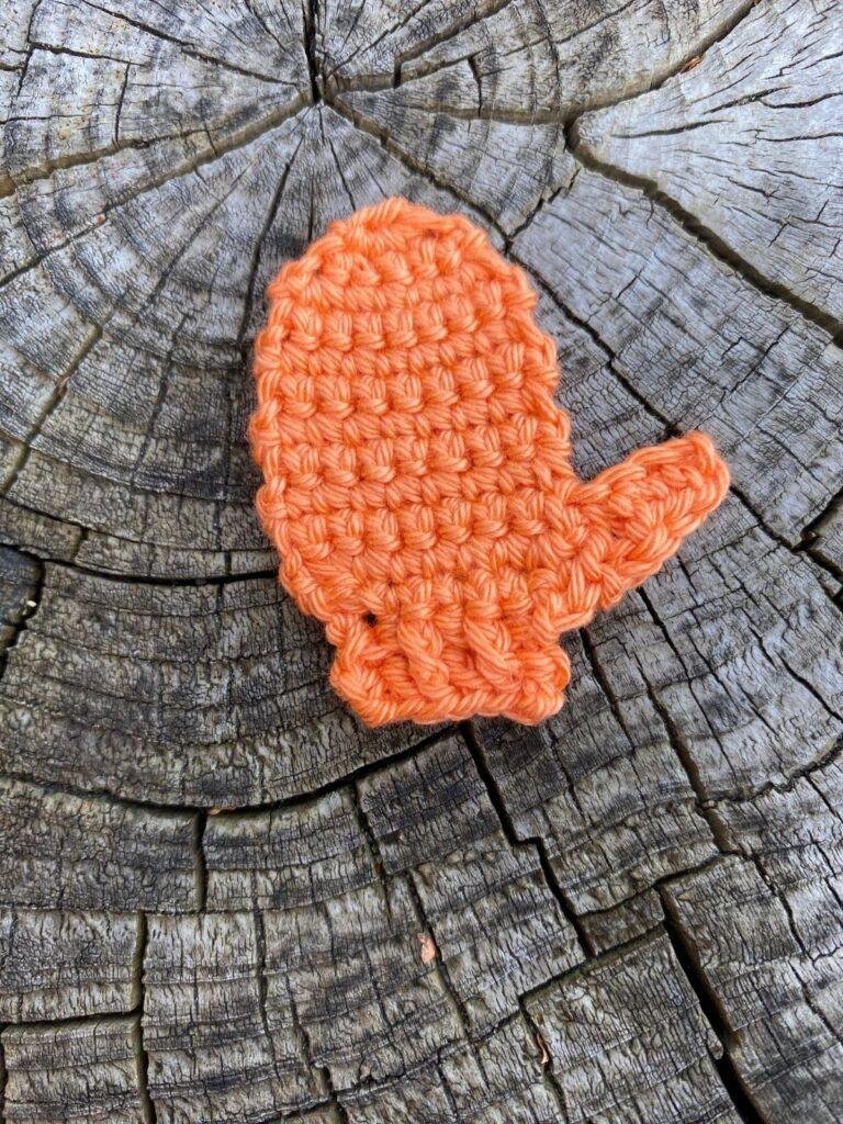 A crochet mitten applique decoration lays on a wooden slice