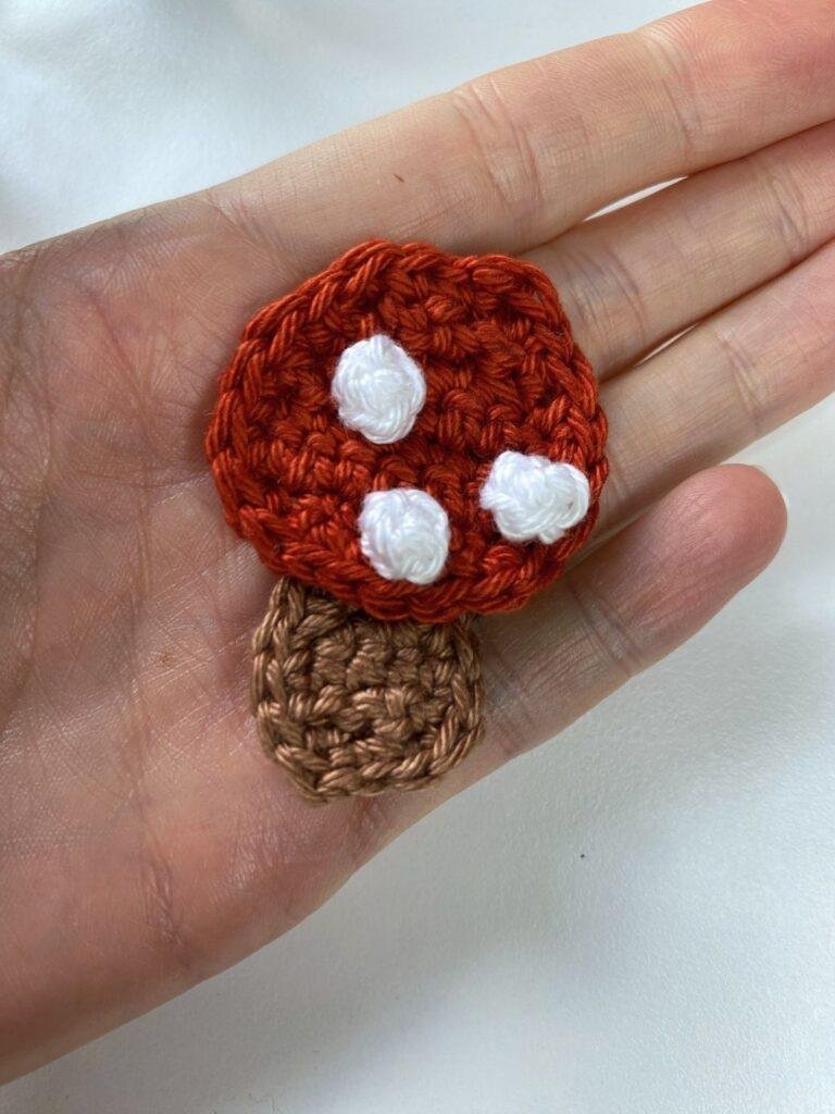 A small crochet toadstool ornament decoration lies flat in a hand