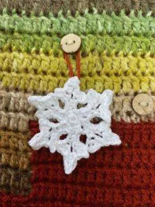 A crochet snowflake decoration hanging a button of a red and green crochet advent calendar