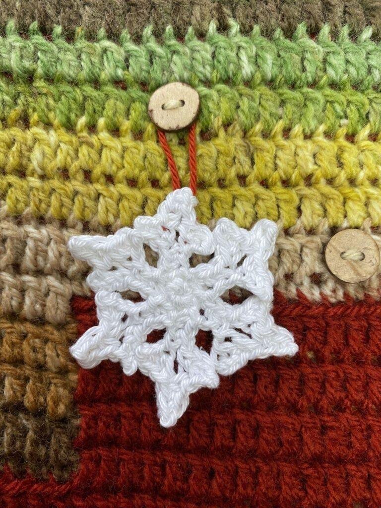 A crochet snowflake decoration hanging a button of a red and green crochet advent calendar