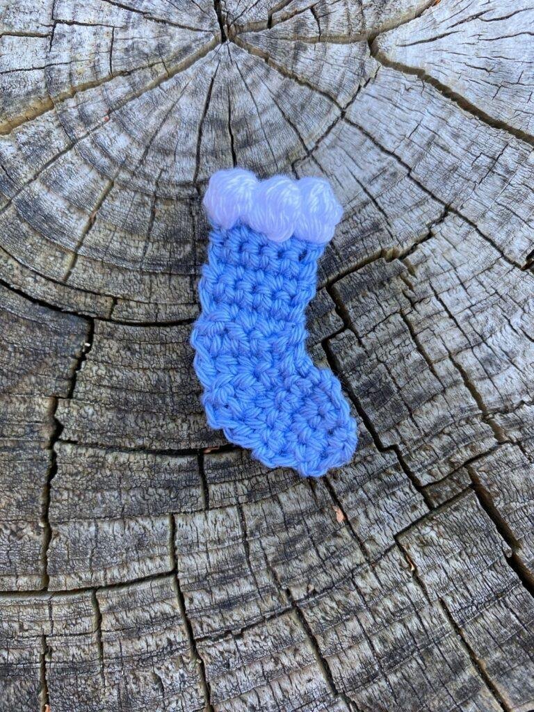 A blue crochet stocking with white top sits on a wooden slice
