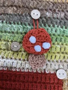 A crochet toadstool hangs on a button on a crochet advent calendar