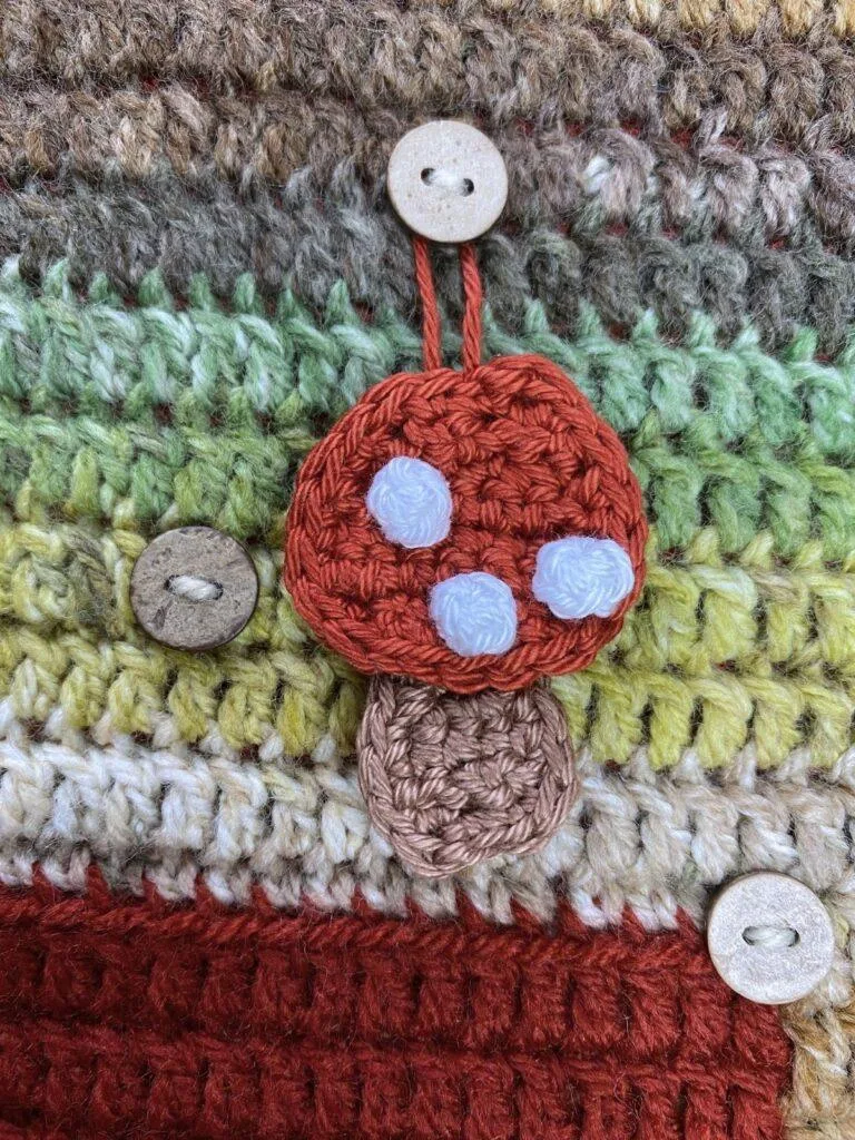 A crochet toadstool hangs on a button on a crochet advent calendar