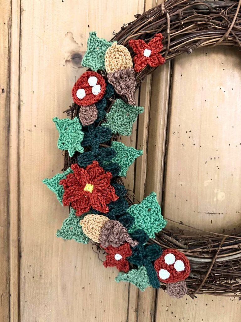 A close up on one side of a crochet wreath featuring leaves, flowers, acorns, and toadstools