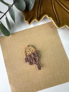 A crochet acorn applique in beige and brown yarn