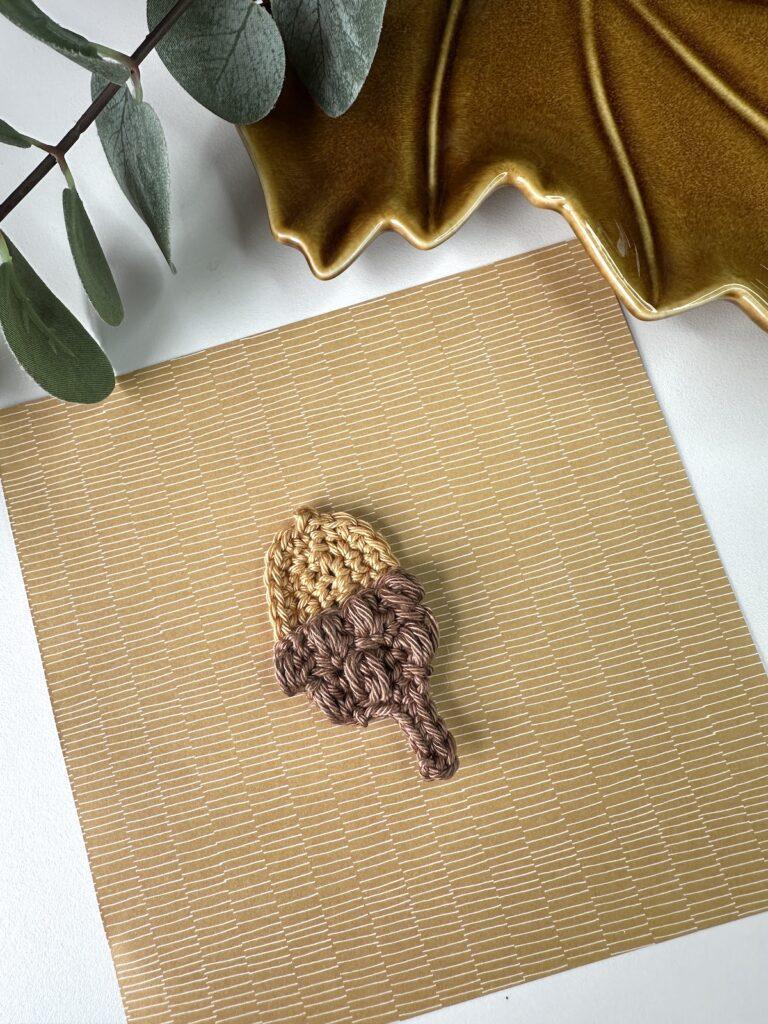 A crochet acorn applique in beige and brown yarn