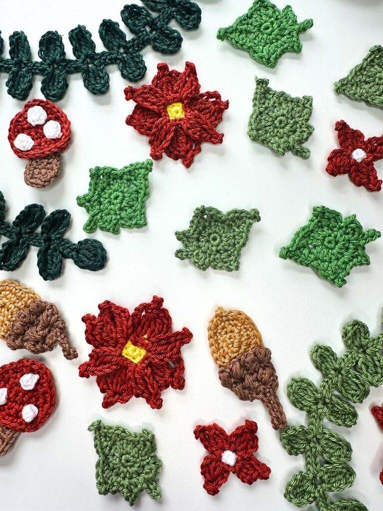 An arrangement of crochet leaves, acorns, flowers and toadstools on a white background. 