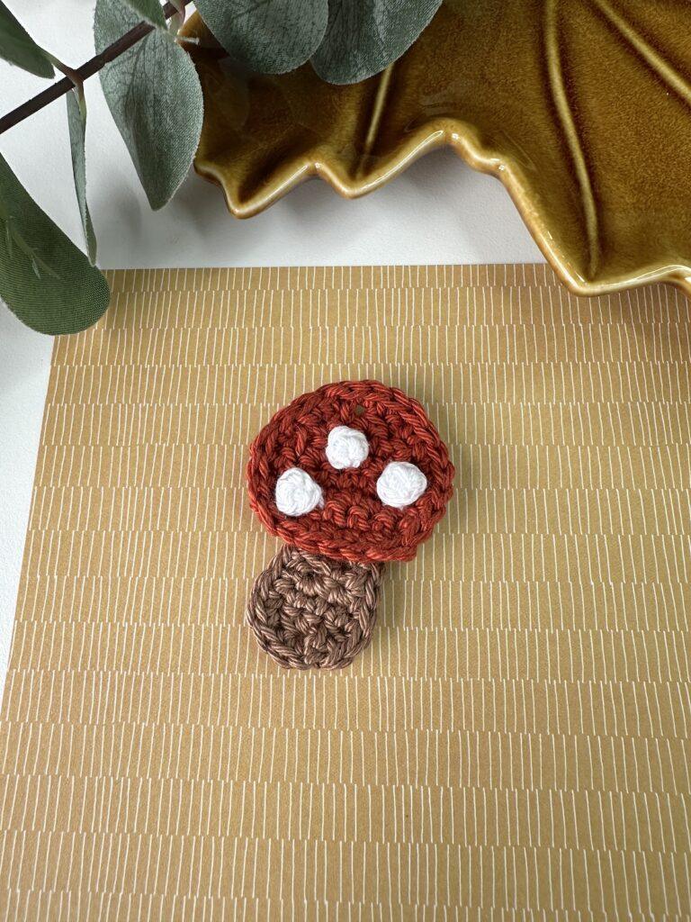A small crochet toadstool applique on a brown paper surface