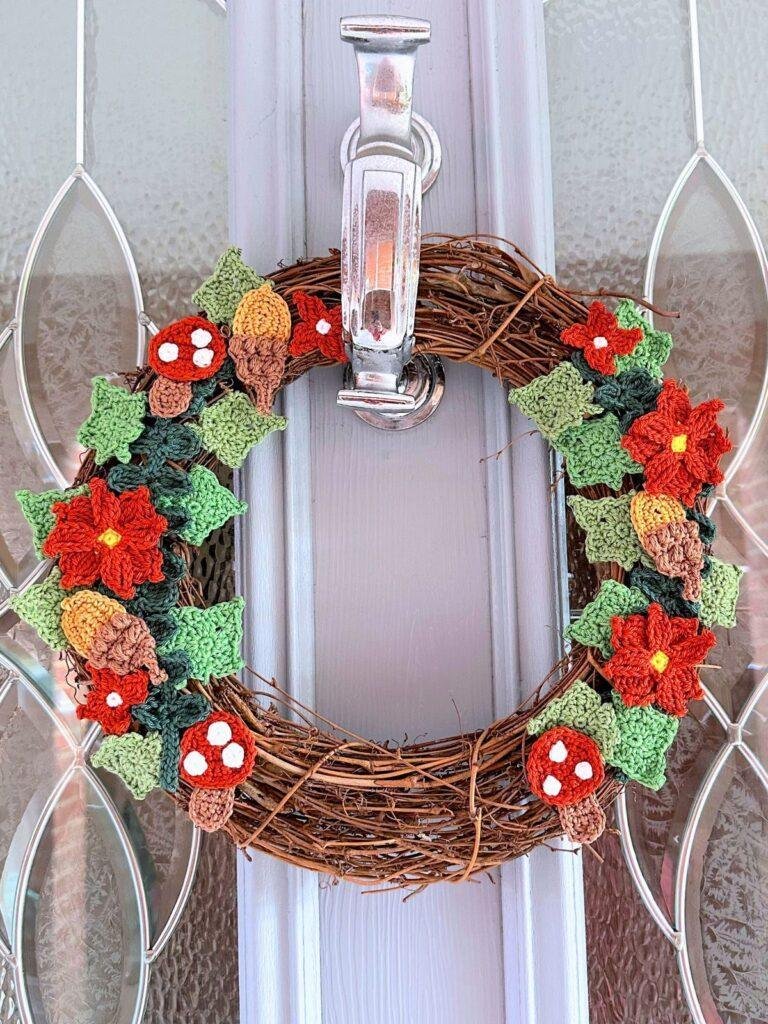 A crochet wreath with toadstools, flowers and leaves hangs on a grey door