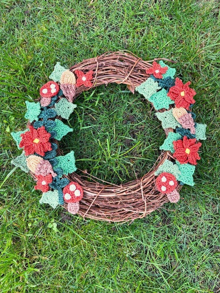A crochet woodland wreath lays on the grass with a rattan base and crochet motifs