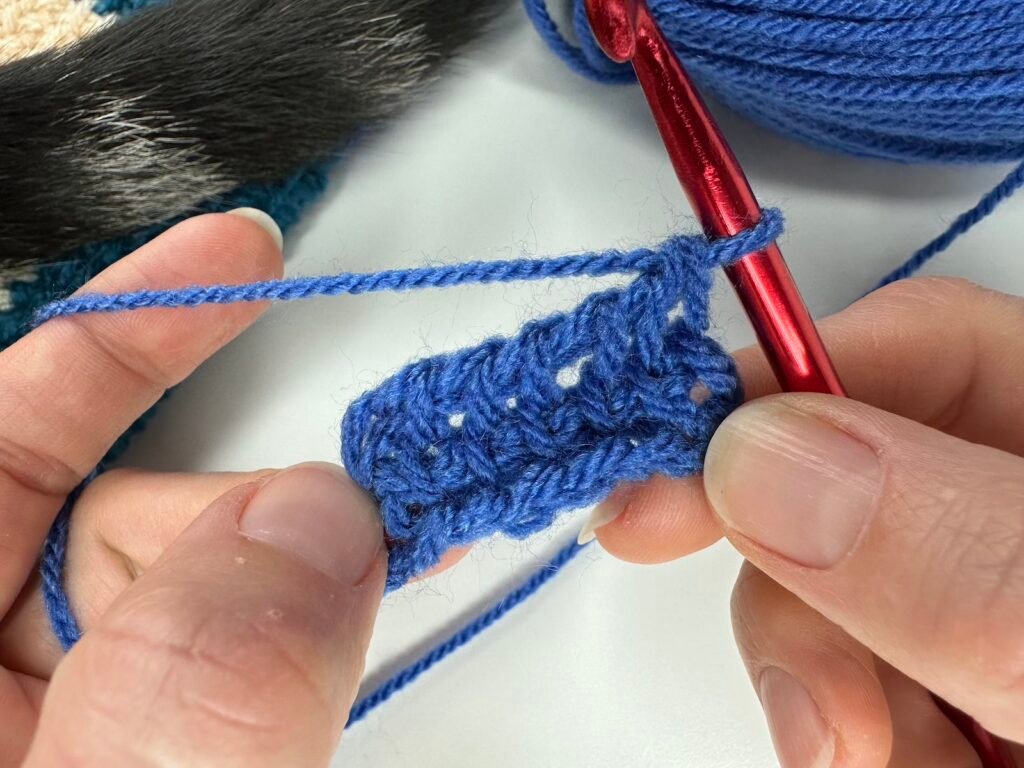 2 hands hold a blue crochet fabric to show a few rows of the first square of Tunisian crochet entrelac