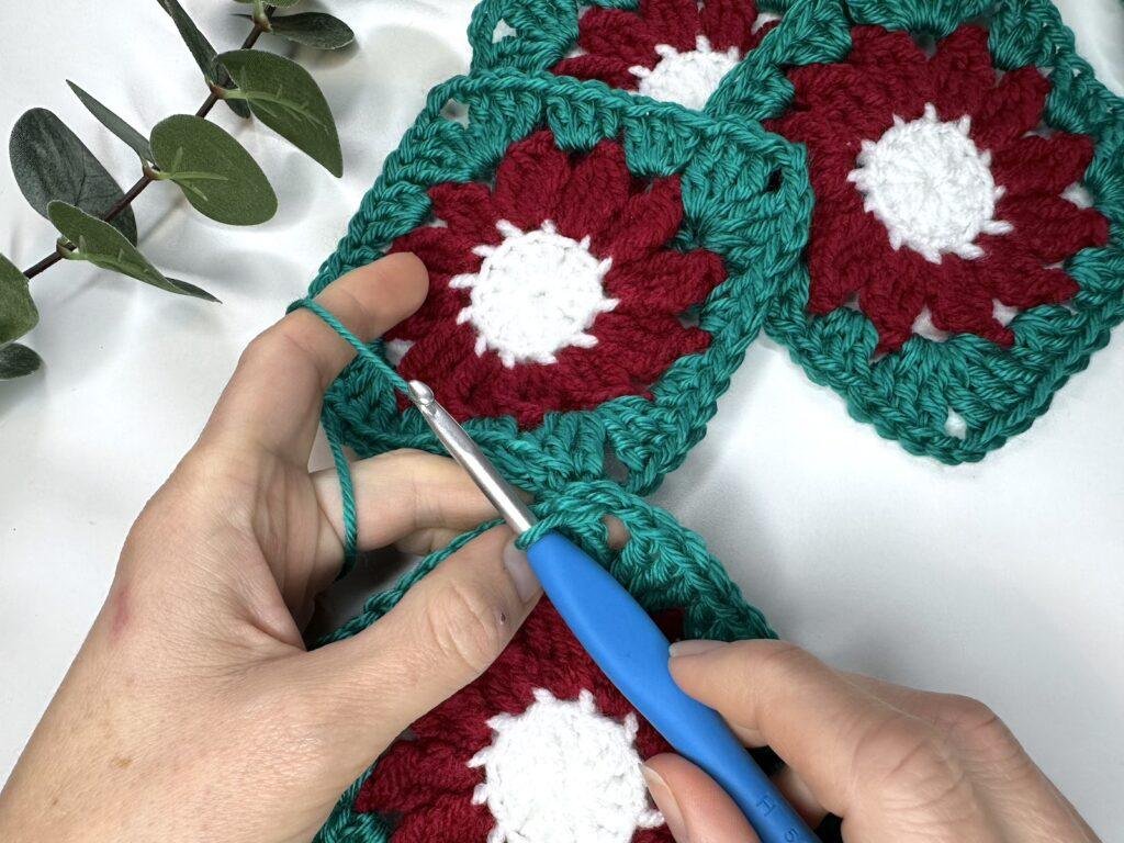 2 hands holding a hook and 2 crochet motifs having just completed a crochet slip stitch seam to join them together