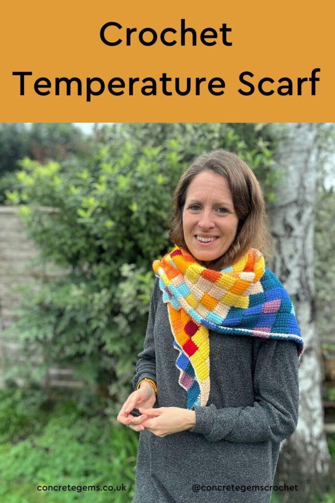 There are words at the top over a yellow background, saying CROCHET TEMPERATURE SCARF. Below there is a photo of a woman in a grey dress standing in a garden, wearing a triangle crochet shawl which is made up of Tunisian Crochet entrelac blocks in lots of different random colours.