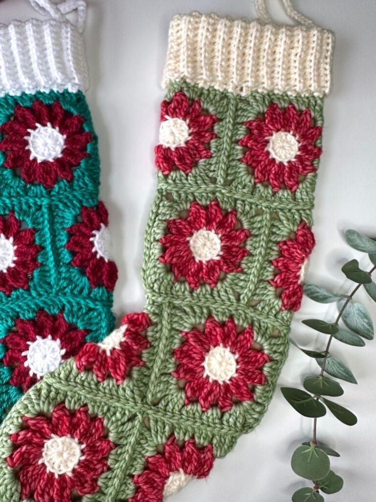 2 crochet stockings are laid out on a white surface with eucalyptus next to them. They are made of flower granny squares