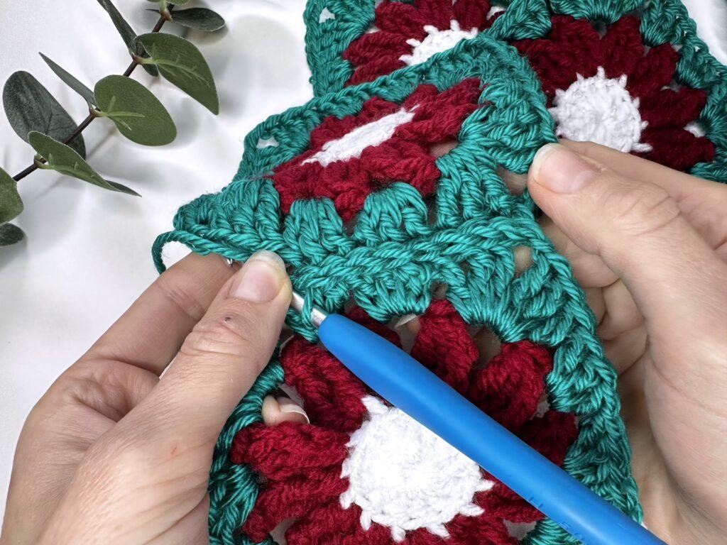 2 hands are holding 2 crochet motifs which are partway through being crocheted together with a slip stitch seam