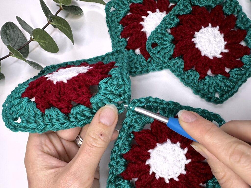 Two hands are using a crochet hook to insert it into the corners of 2 crochet flower motifs