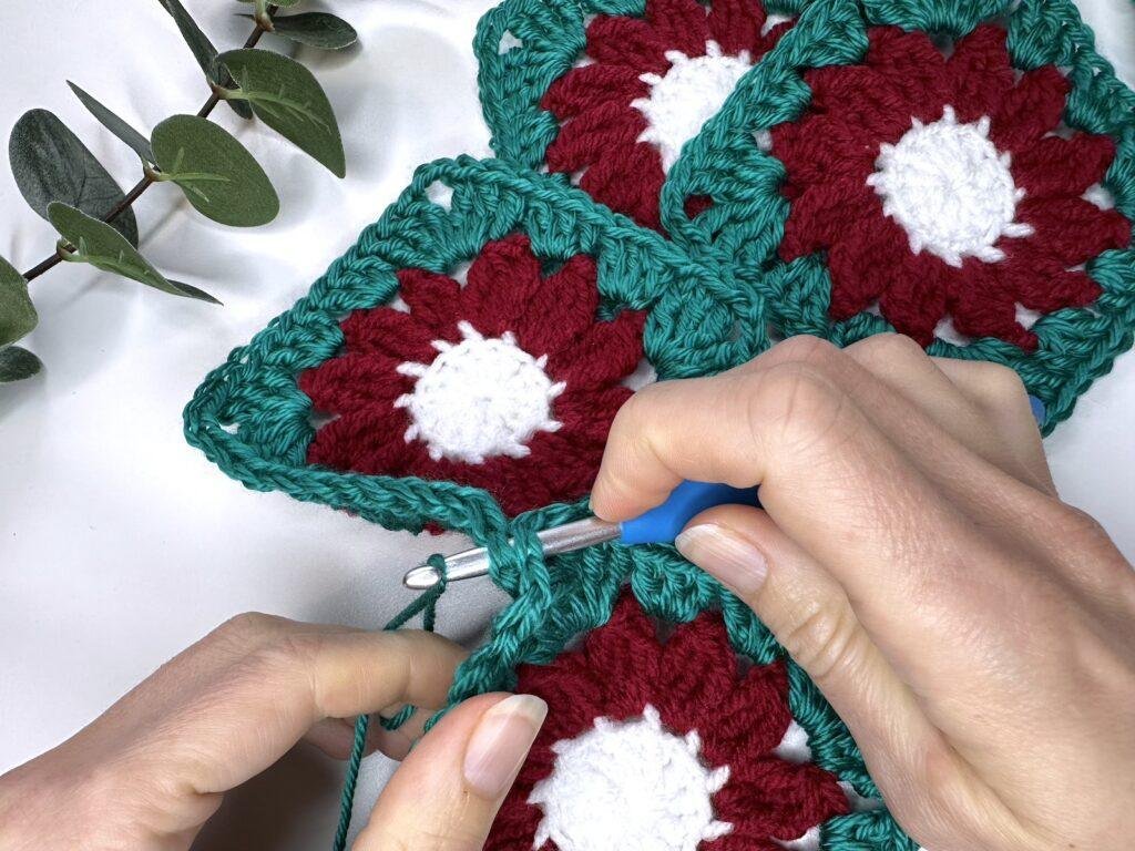 2 hands are now wrapping yarn around the hook which is still through the corners of the 2 crochet motifs