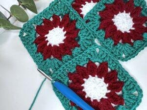 Two crochet granny squares have just been joined with a slip stitch seam in green and a further granny square is to the side.