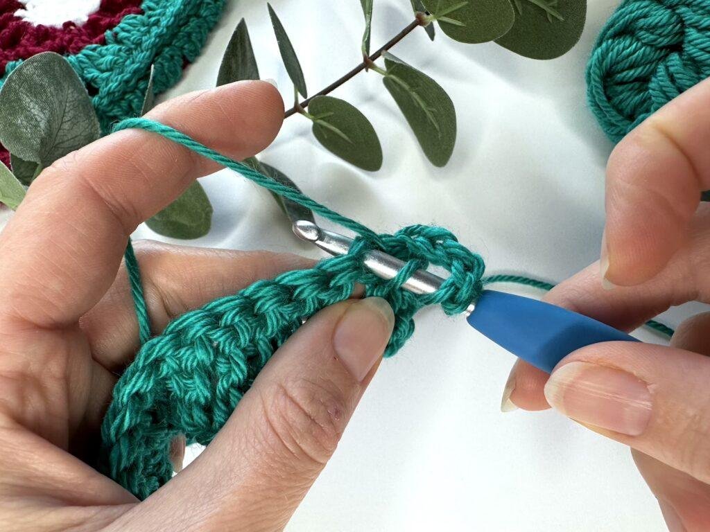 2 hands are inserting a crochet hook into a stitch to make a treble crochet stitch