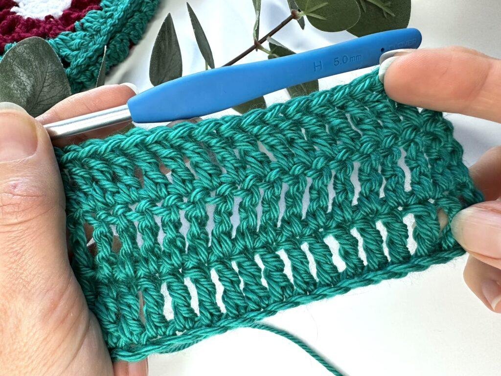 A swatch of crochet treble stitches in green yarn, held in 1 hands