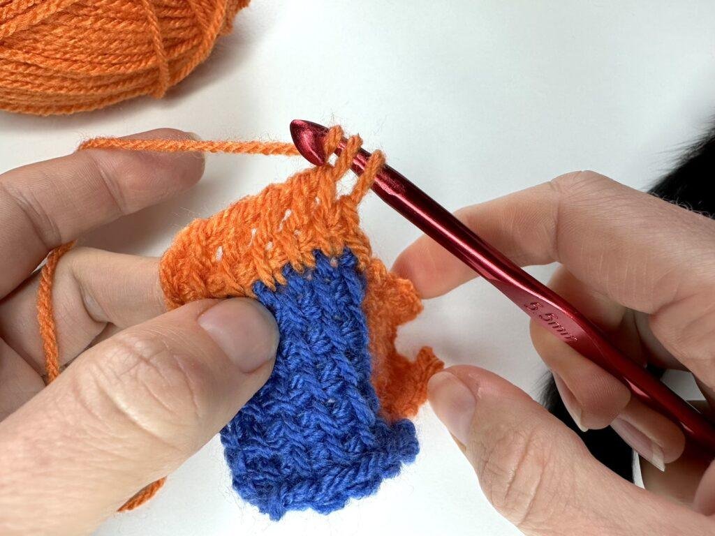 2 hands are holding a small crochet sample of Tunisian crochet entrelac, as they work a return pass