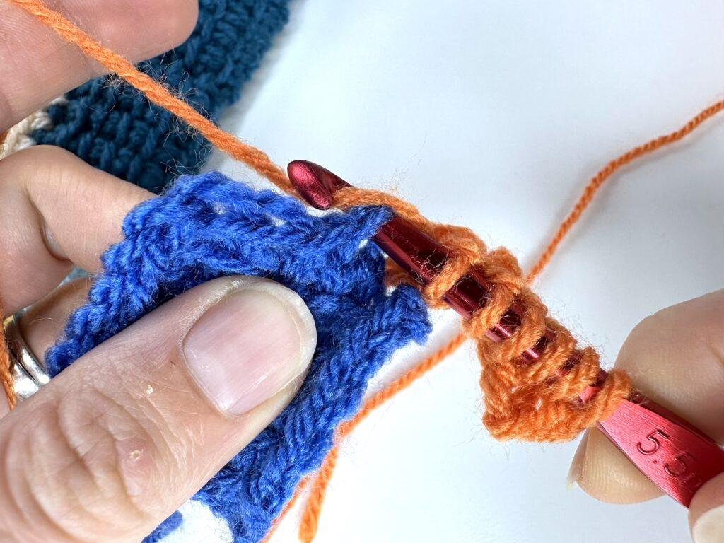 2 hands are crocheting a Tunisian crochet entrelac initial square and working on joining it to the adjacent block