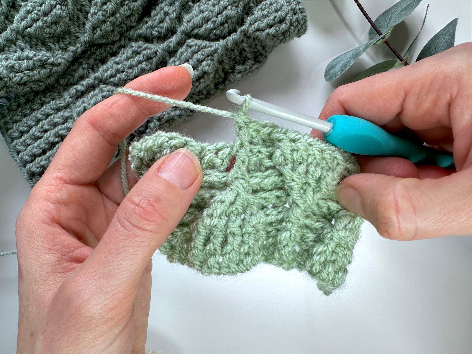 A person is crocheting a front post double crochet in green yarn
