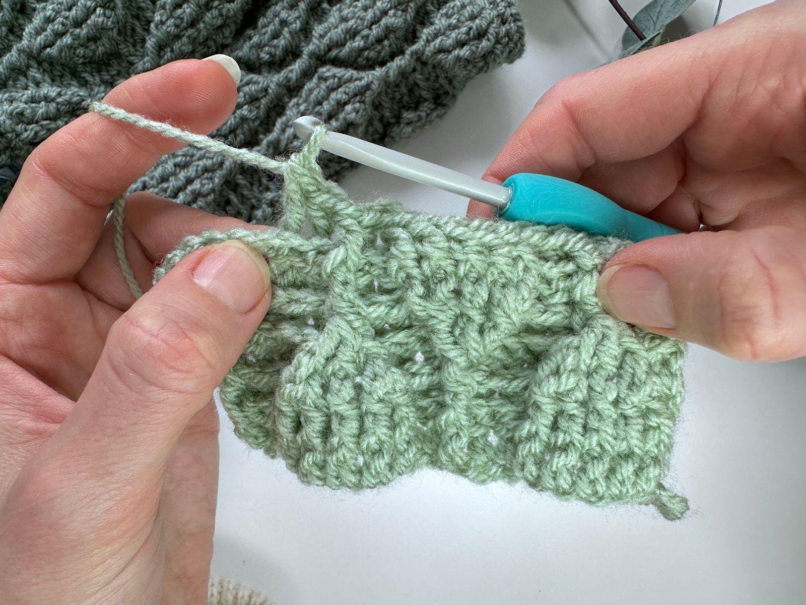 2 hands are crocheting back post double crochet to create a trailing leaves stitch pattern in green yarn