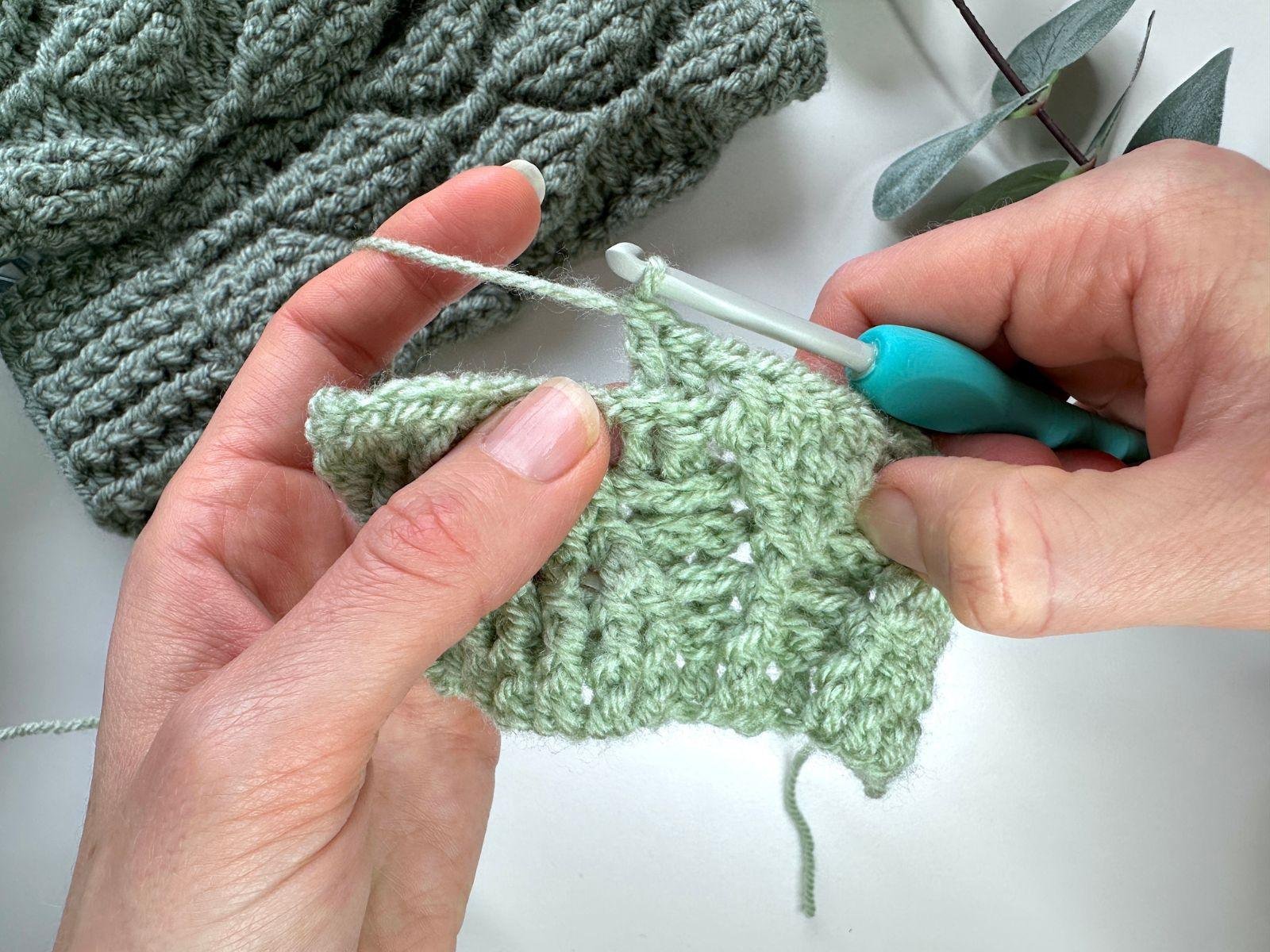 2 hands holding crochet hook and green textured crochet fabric making stitches