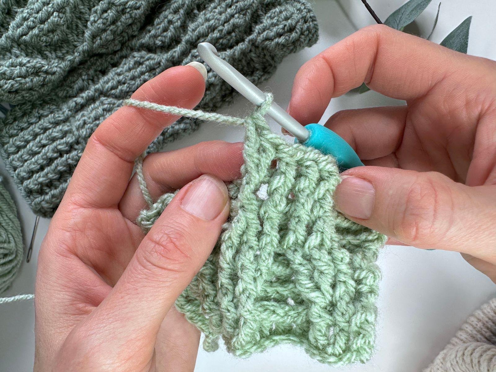 2 front post double crochet stitches worked into the same stitch are shown on a green crochet fabric
