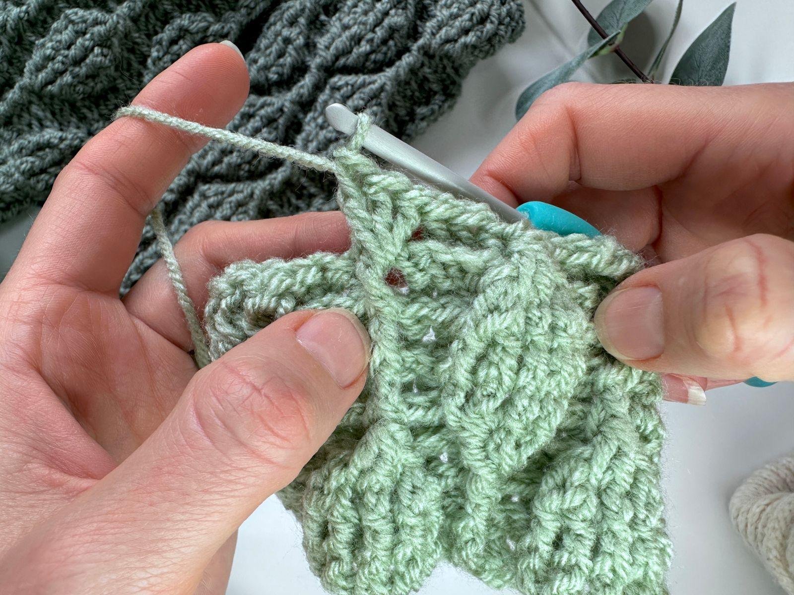 3 front post double crochet are being made in the same stitch in green yarn with 2 hands and a crochet hook