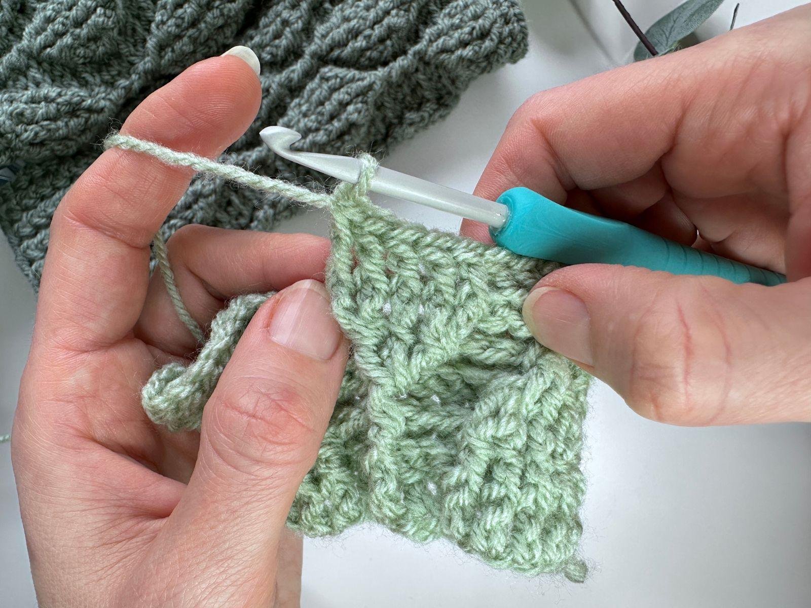 2 hands hold a sample of green textured crochet, having just made 5 front post double crochet stitches