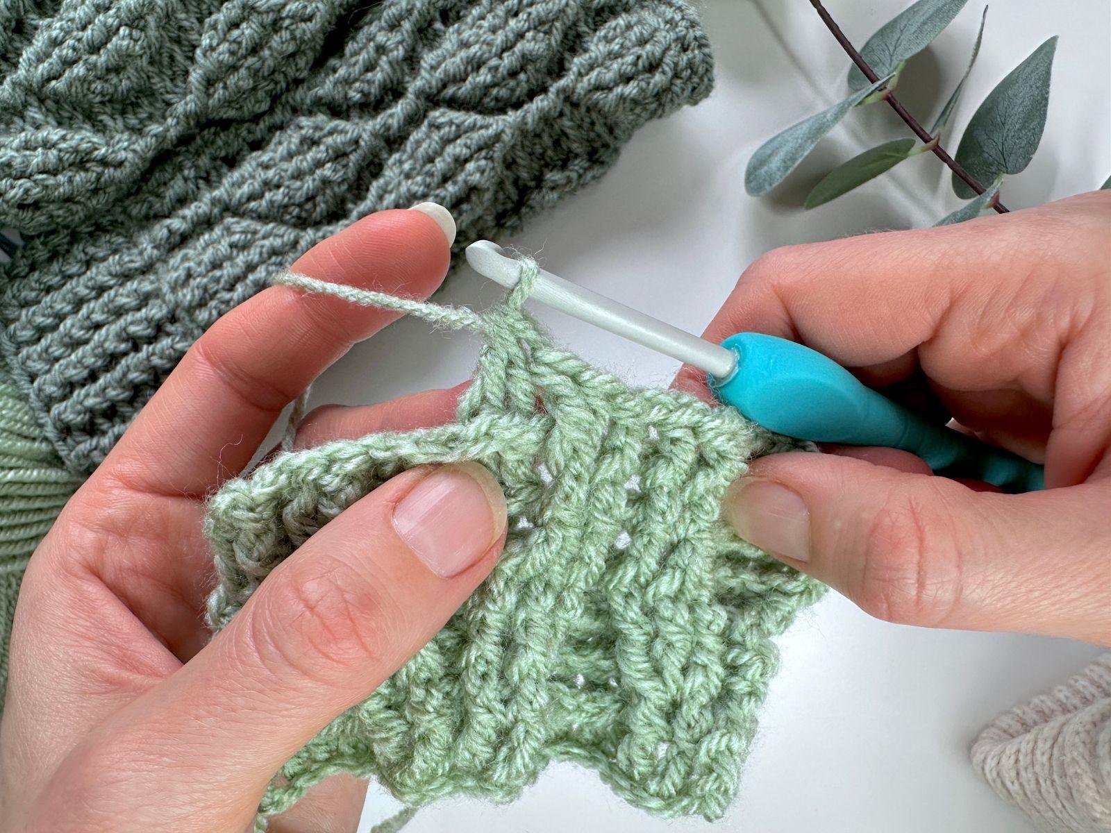 2 hands hold a crochet fabric sample showing a completed back post double crochet 2 together stitch