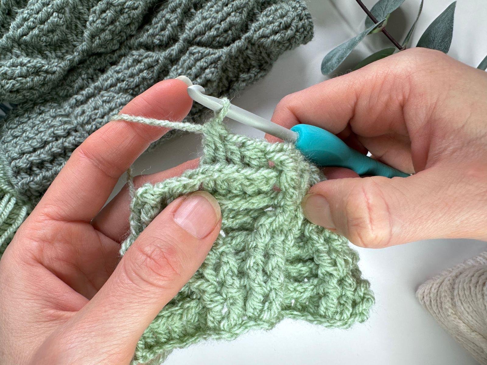 2 hands hold a crochet sample of textured post stitches using green yarn