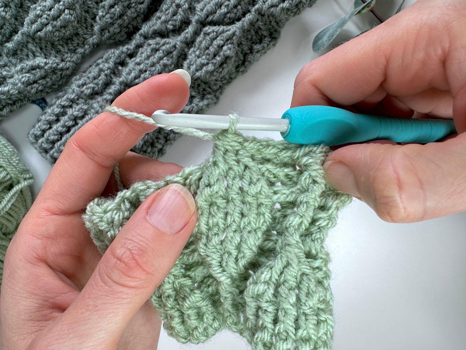 the top of the crochet leaf motif has just been completed by a crochet hook and 2 hands