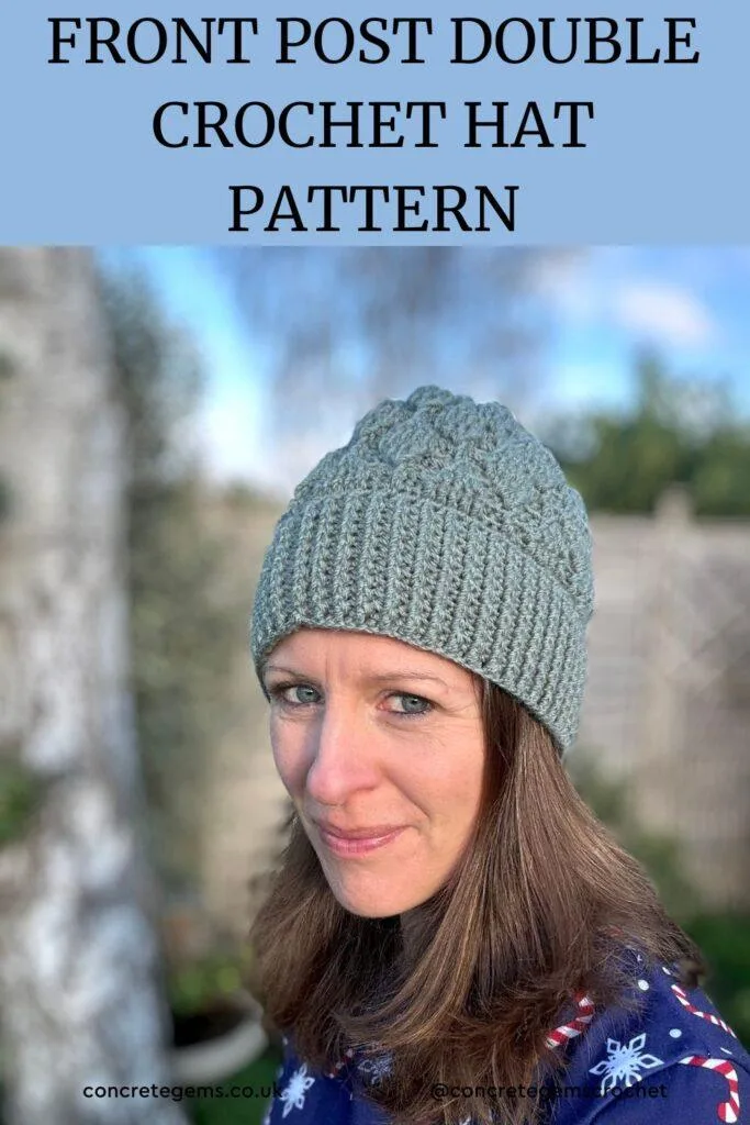 A lady stands in a garden wearing a green crochet beanie with crochet leaves running up the hat.