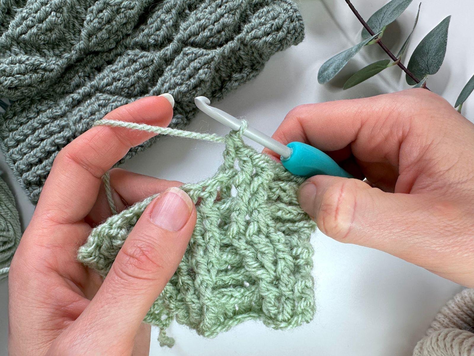 2 hands work a back post double crochet stitch using green yarn