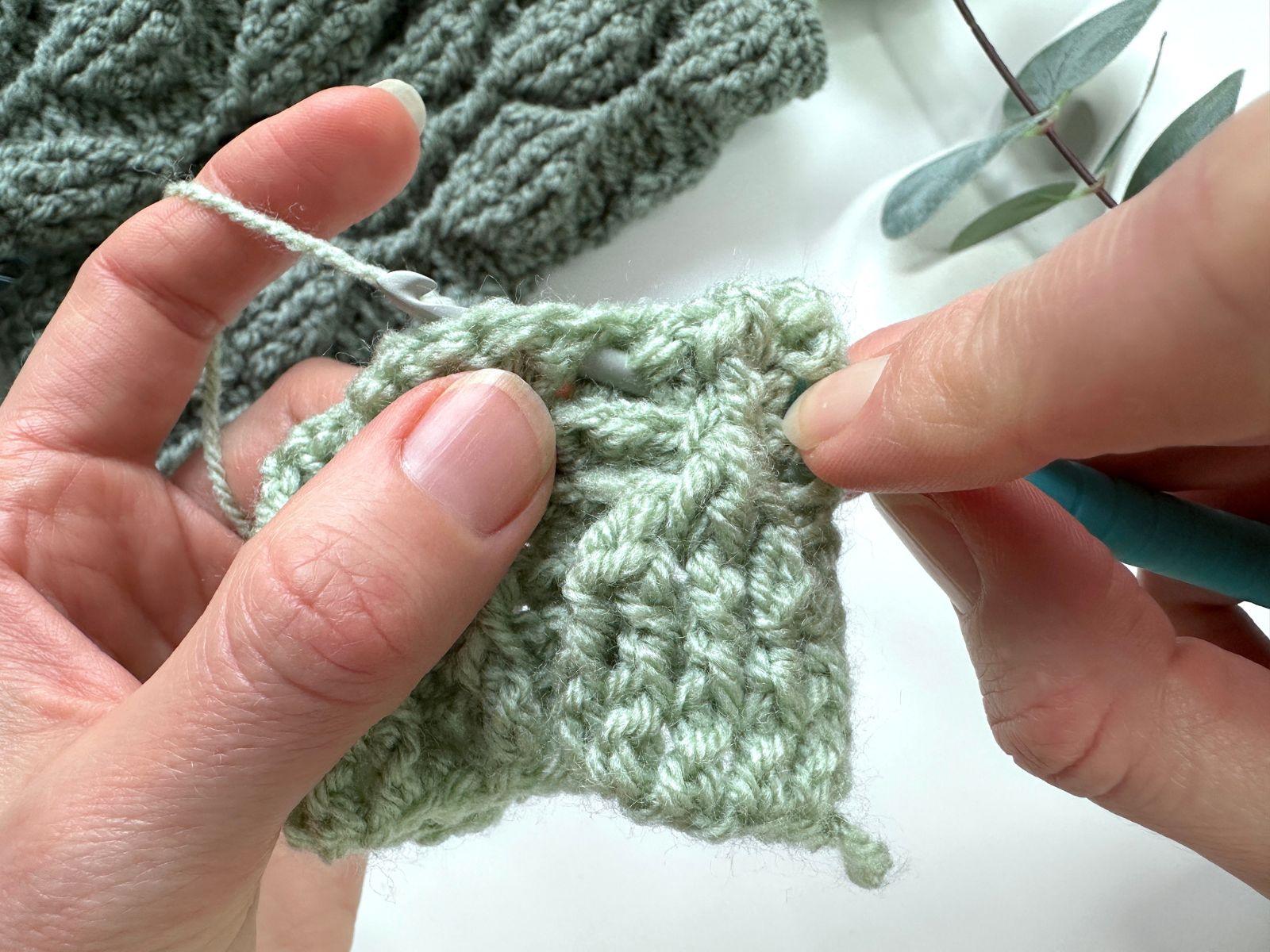 2 hands are showing where the hook has been inserted in a stitch from the back