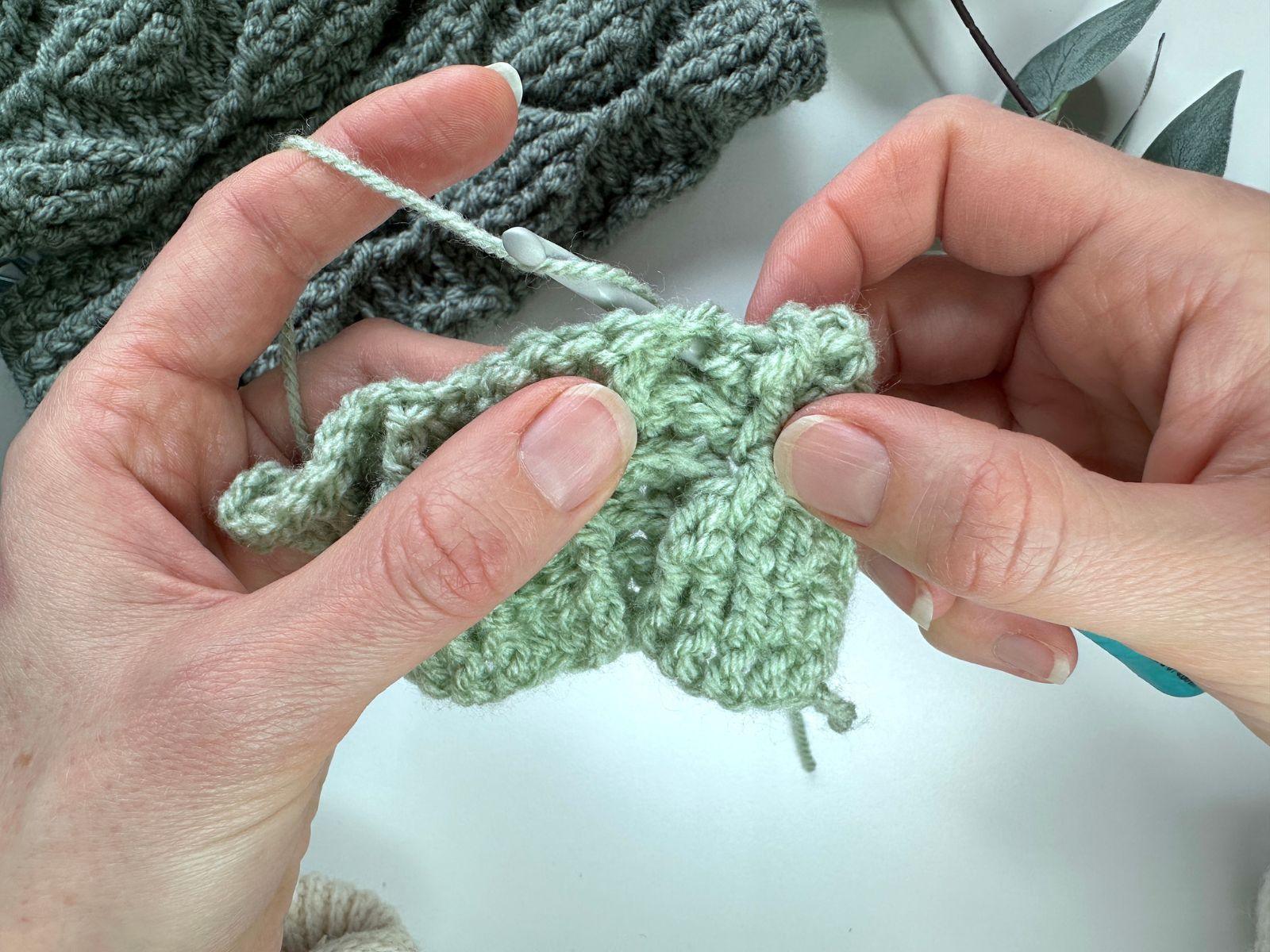 2 hands are holding a crochet hook and crochet swatch and are working a bpdc
