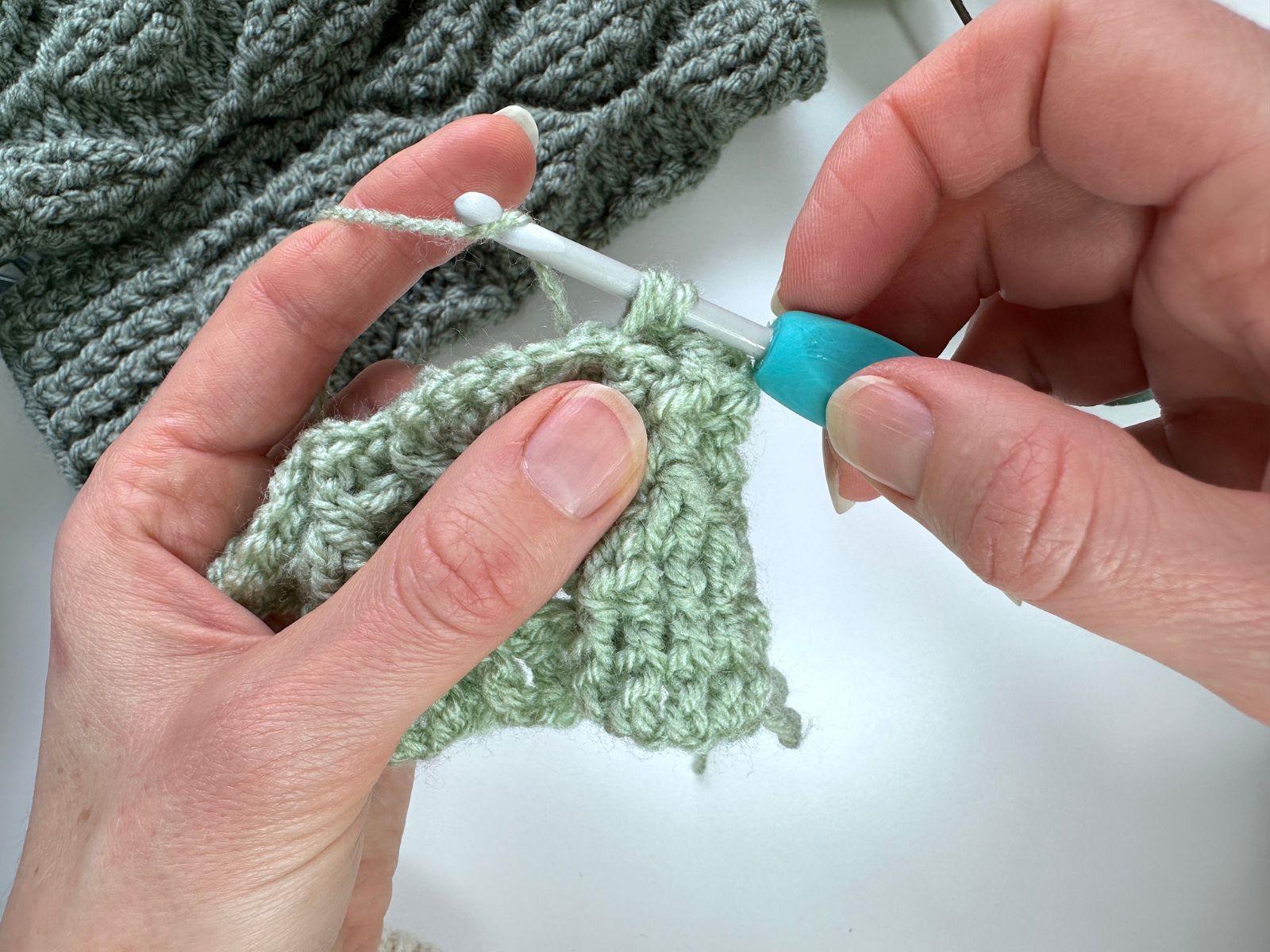 2 hands are crocheting a back post double crochet with green yarn