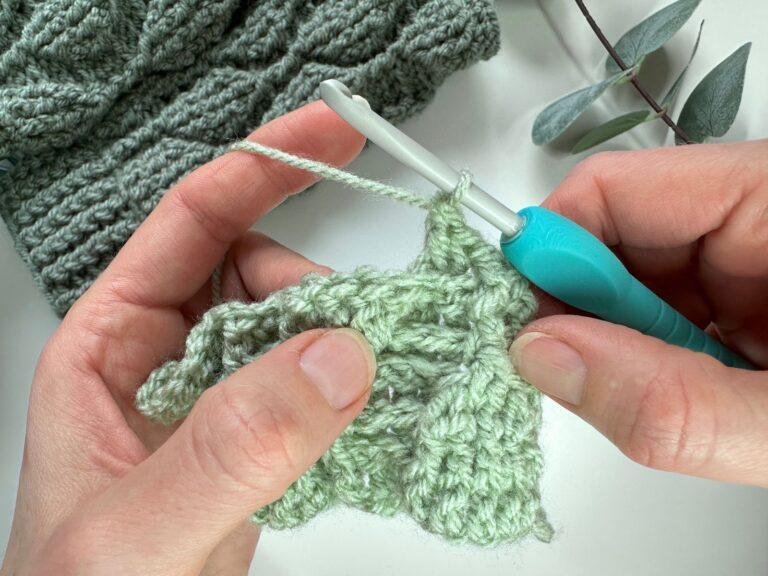 2 hands hold a green crochet sample showing a completed back post double crochet stitch