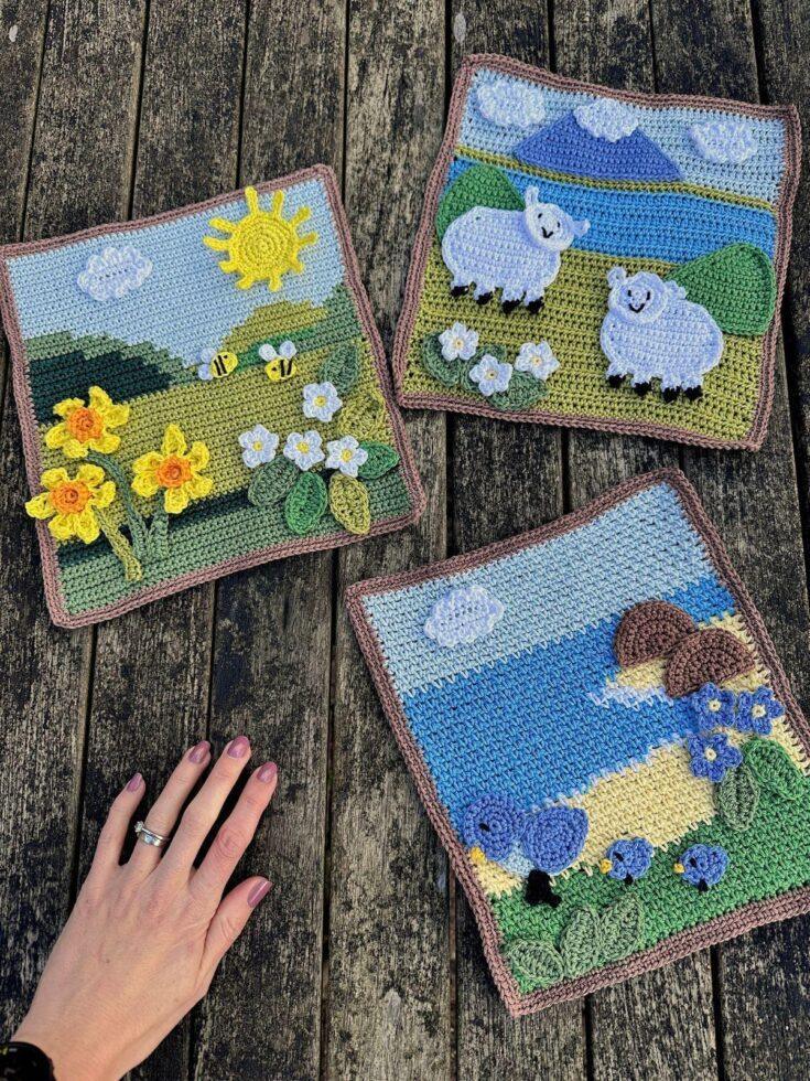 3 crochet springs landscapes are laid out on a wooden table with a hand next to them.