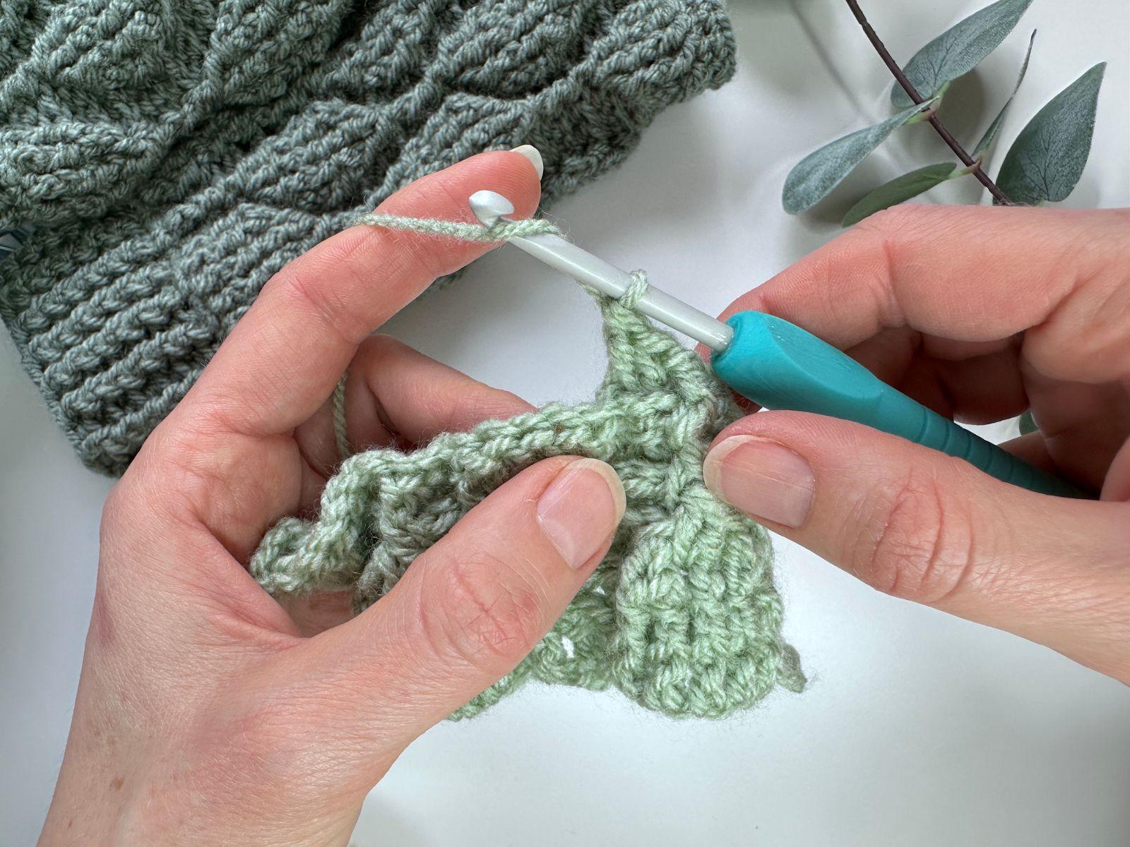 2 hands hold a sample of green crochet and are wrapping the yarn around the hook for a stitch