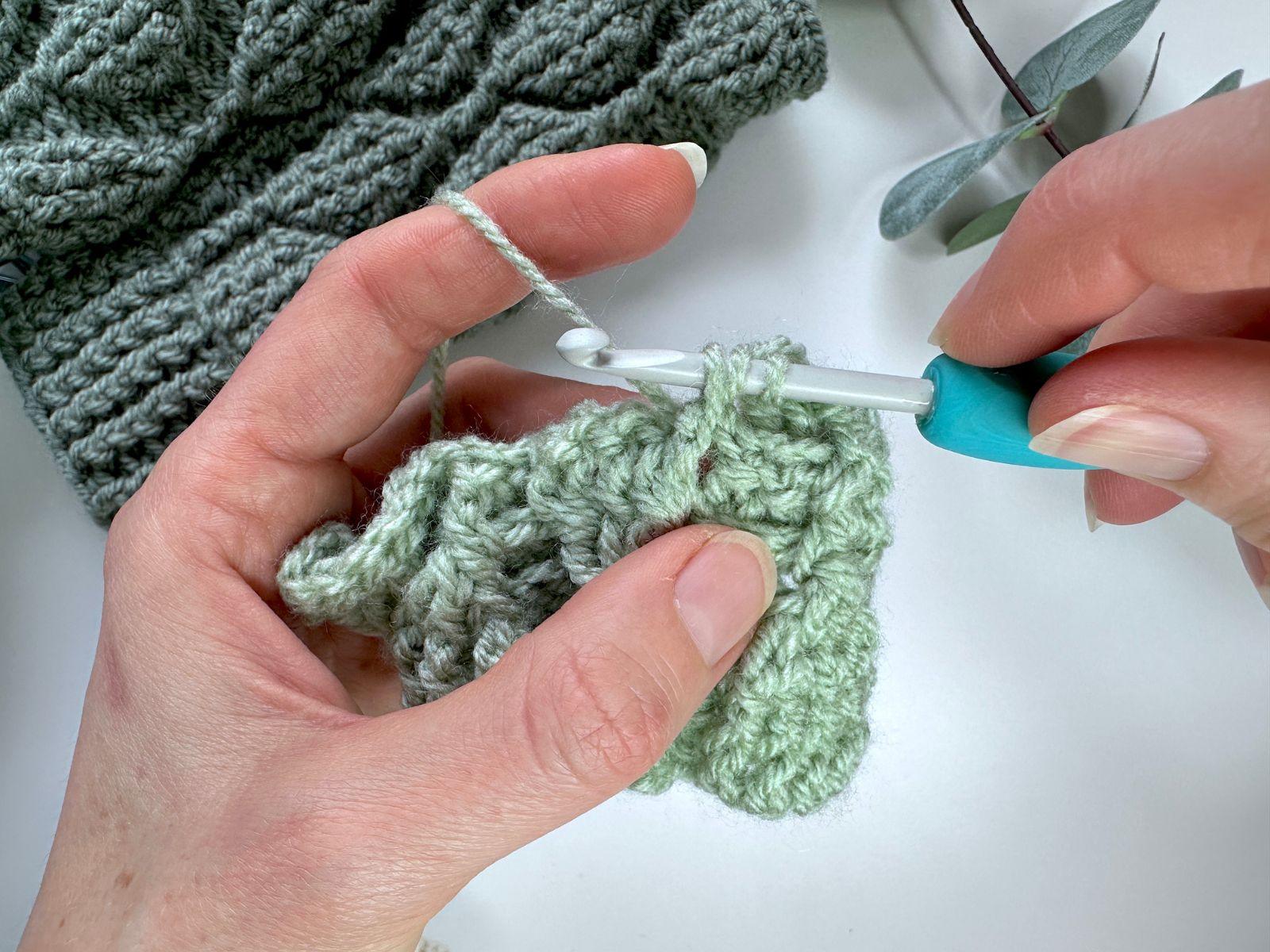 A person holds a green crochet sample to make a front post double crochet stitch