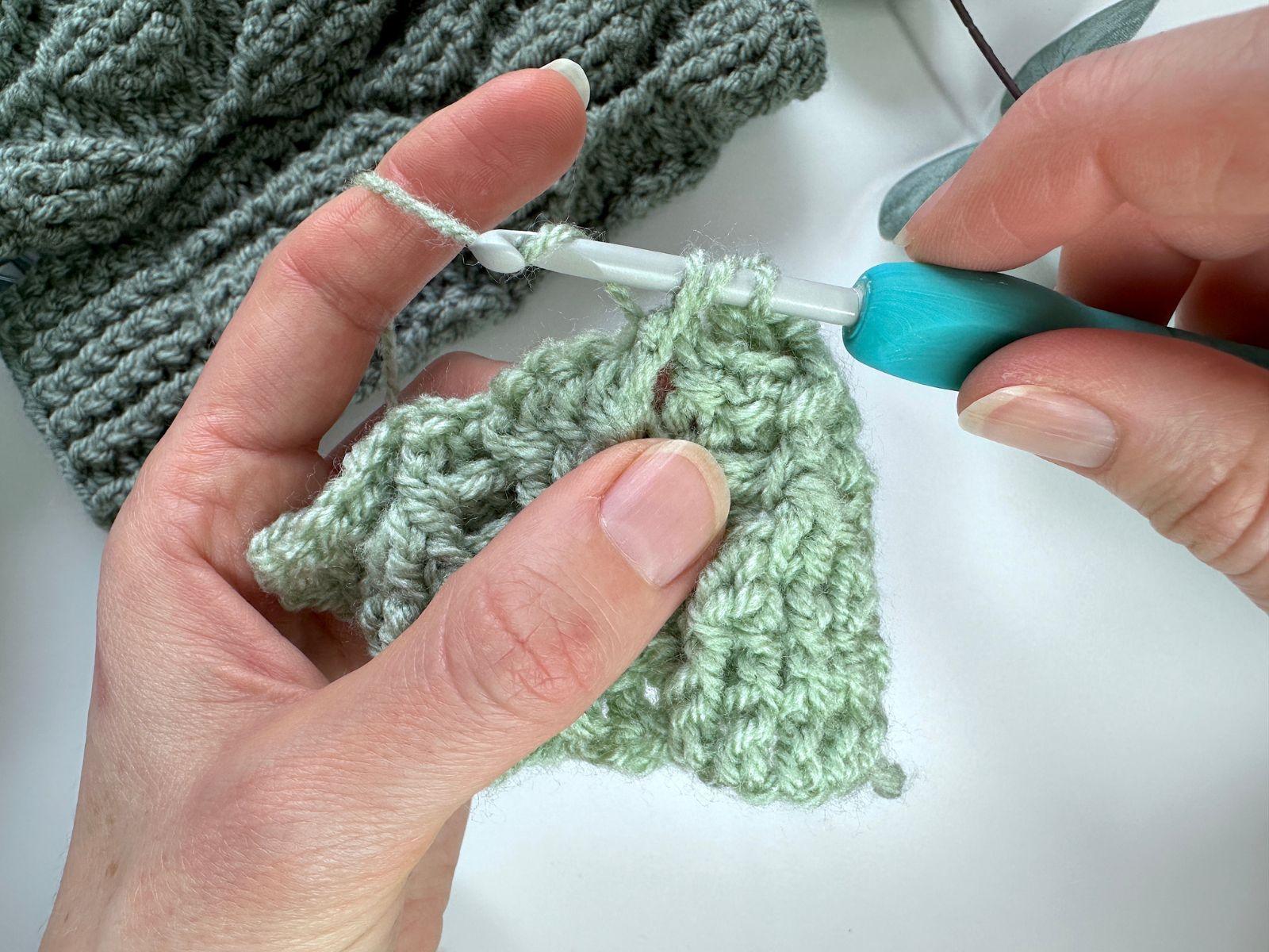 2 hands are wrapping the yarn around a hook partway through a crochet stitch