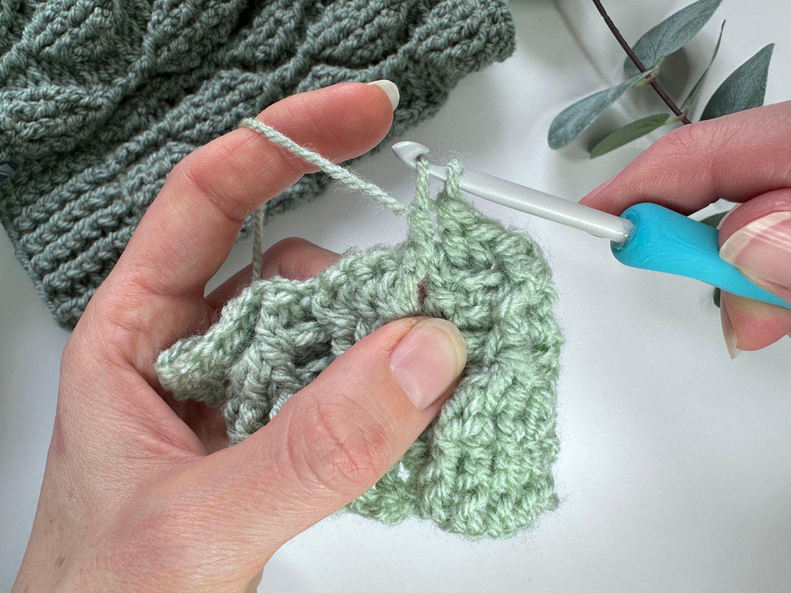 2 hands hold a crochet sample and a green hook