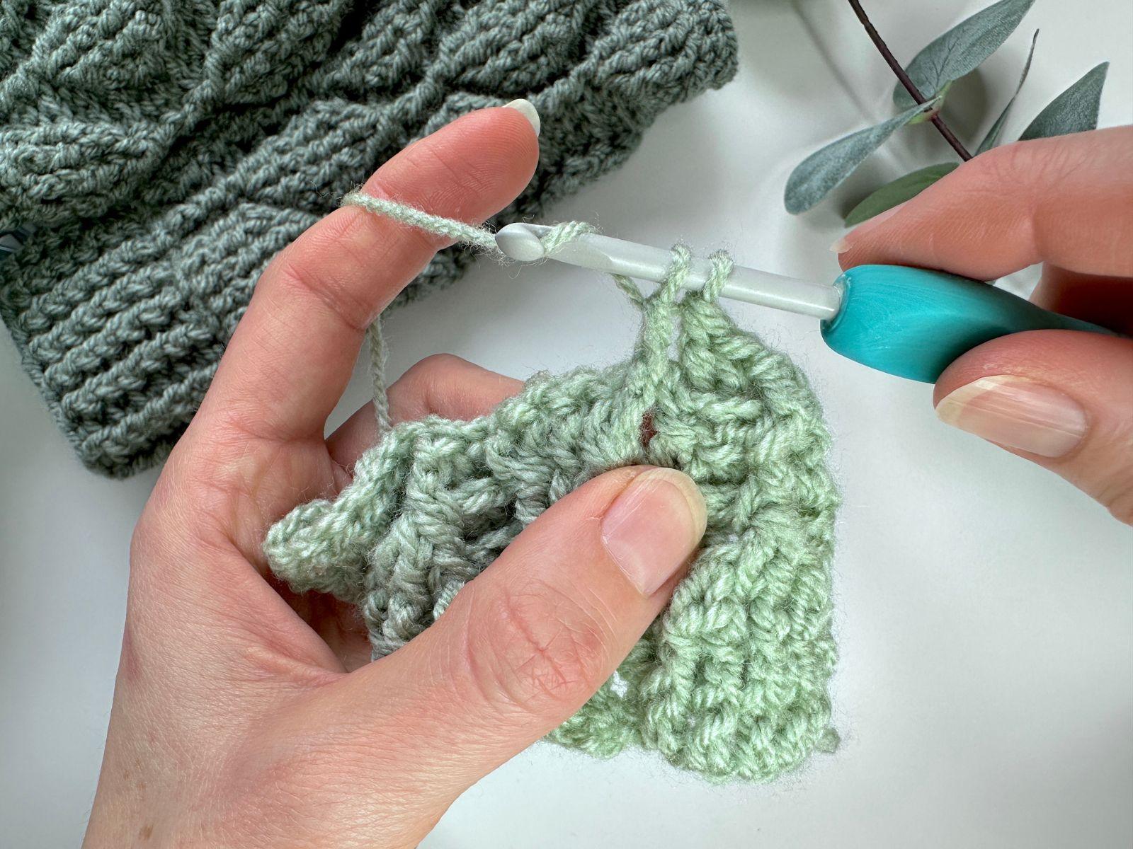 2 hands hold a crochet swatch and hook and make a post stitch