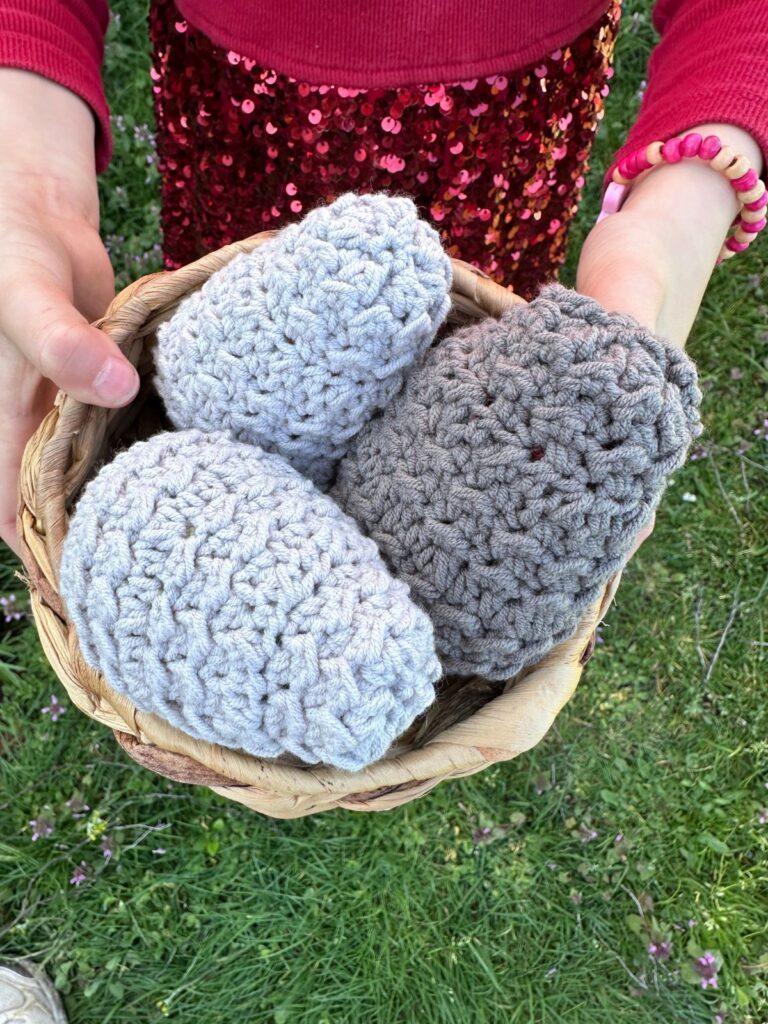 A child is a red dress holds a wicker bowl of grey crochet eggs with beautiful texture